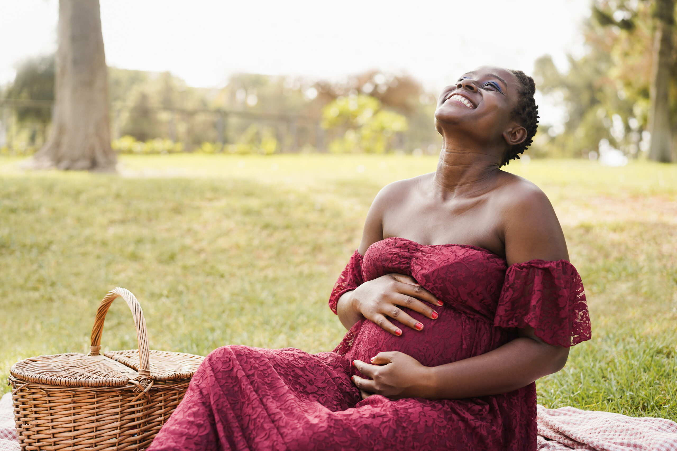 Happy african pregnant woman touching her belly outdoor at city park – Focus on face