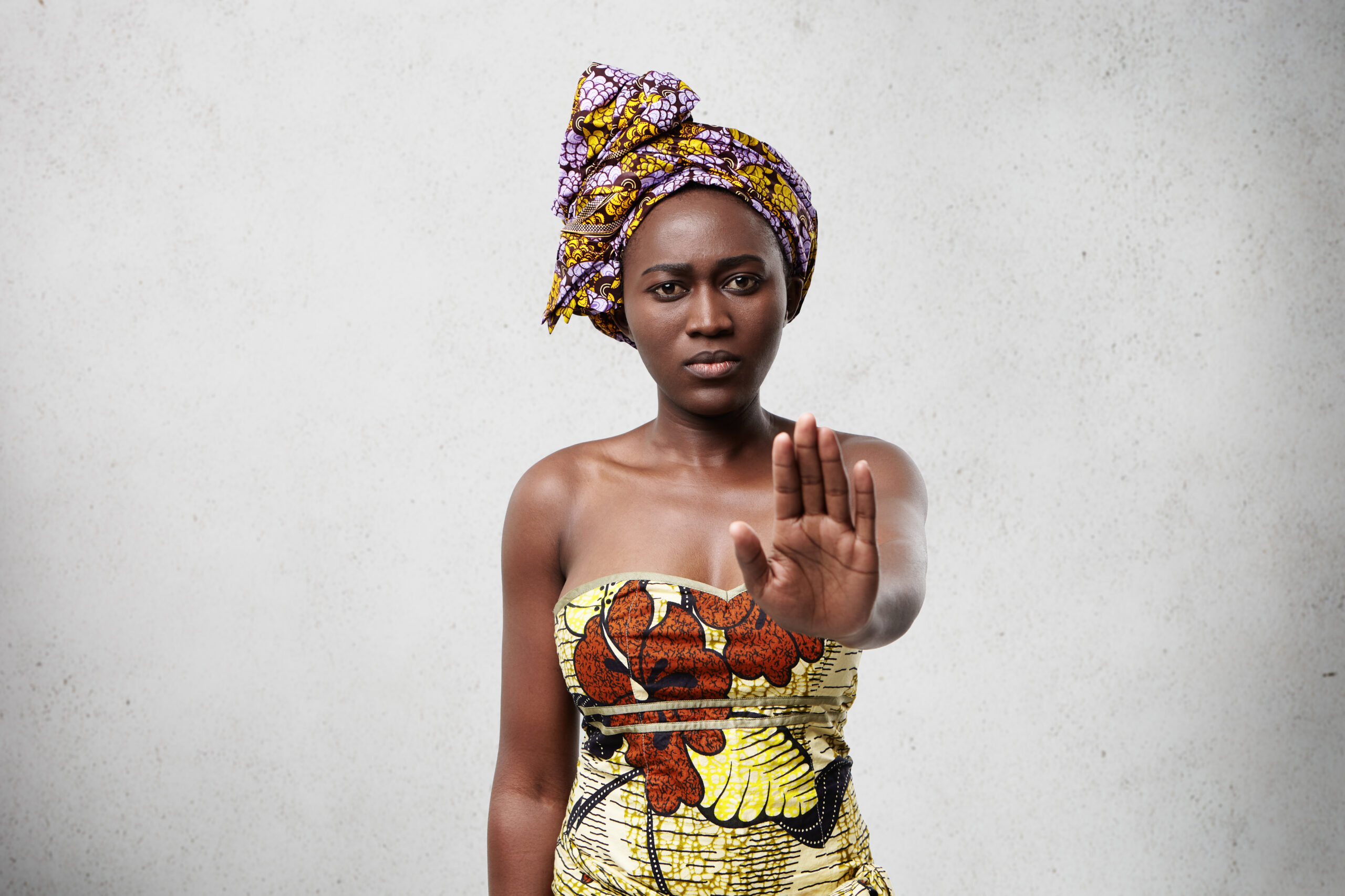 Stop it! African woman with dark smooth skin wearing traditional clothes showing her palm denying not to do something. Confident dark-skinned female showing no gesture. Veto and demand concept